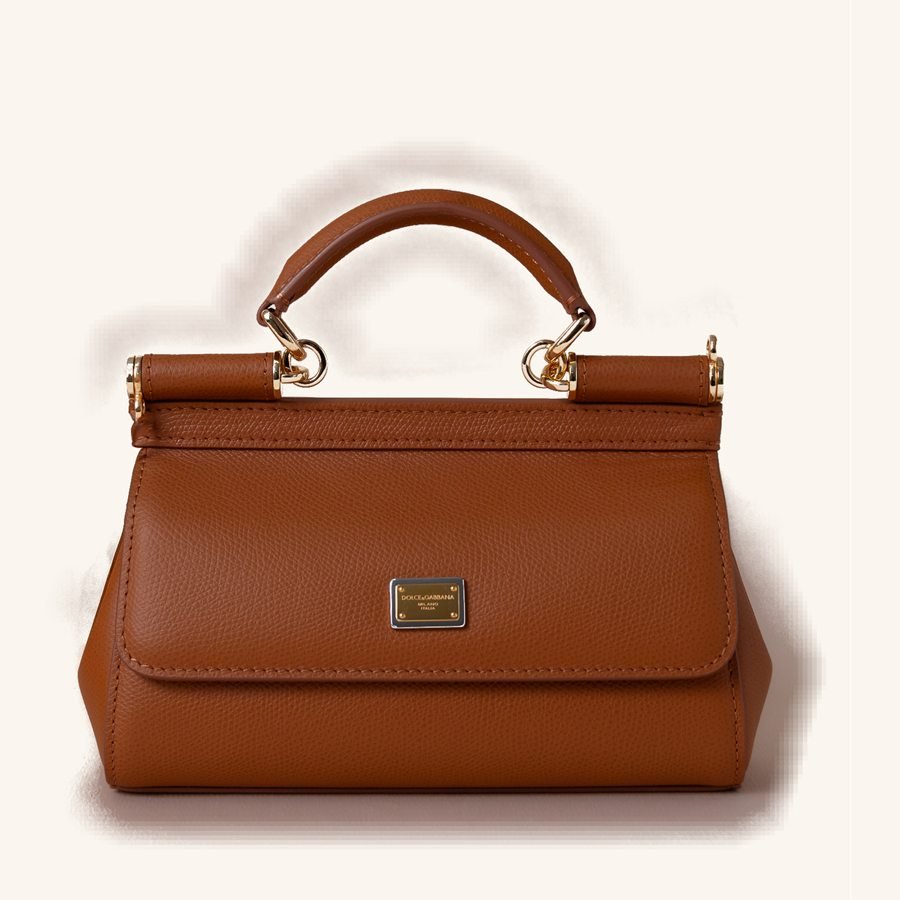 Bolsa caramelo em couro granulado, alça superior arqueada, ferragem dourada e placa metálica centrada.